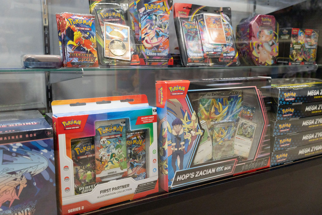 Sealed Pokémon TCG boxes, tins, and blister packs in a display case.